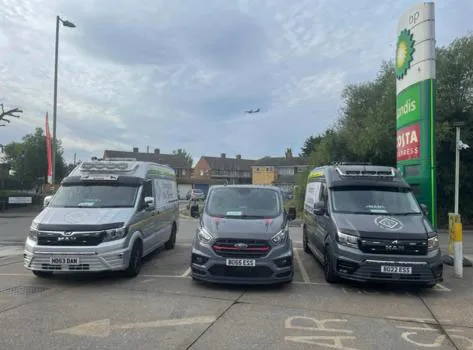 three vans parked in a parking lot next to a gas station